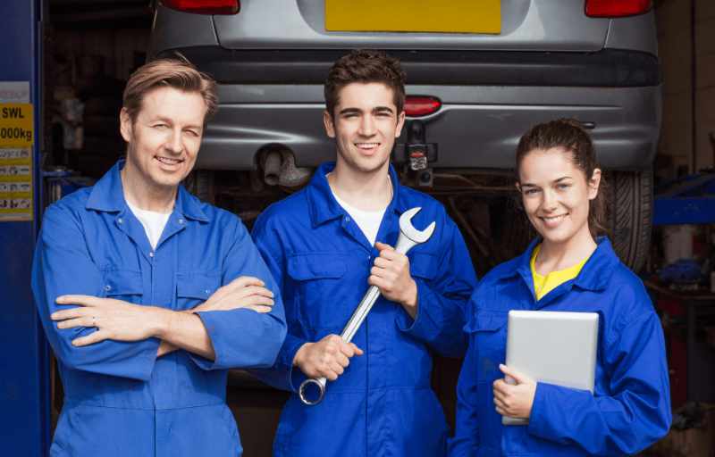 Automechaniker und Lehrlinge in blauen Arbeitsanzug vor Werkstatt
